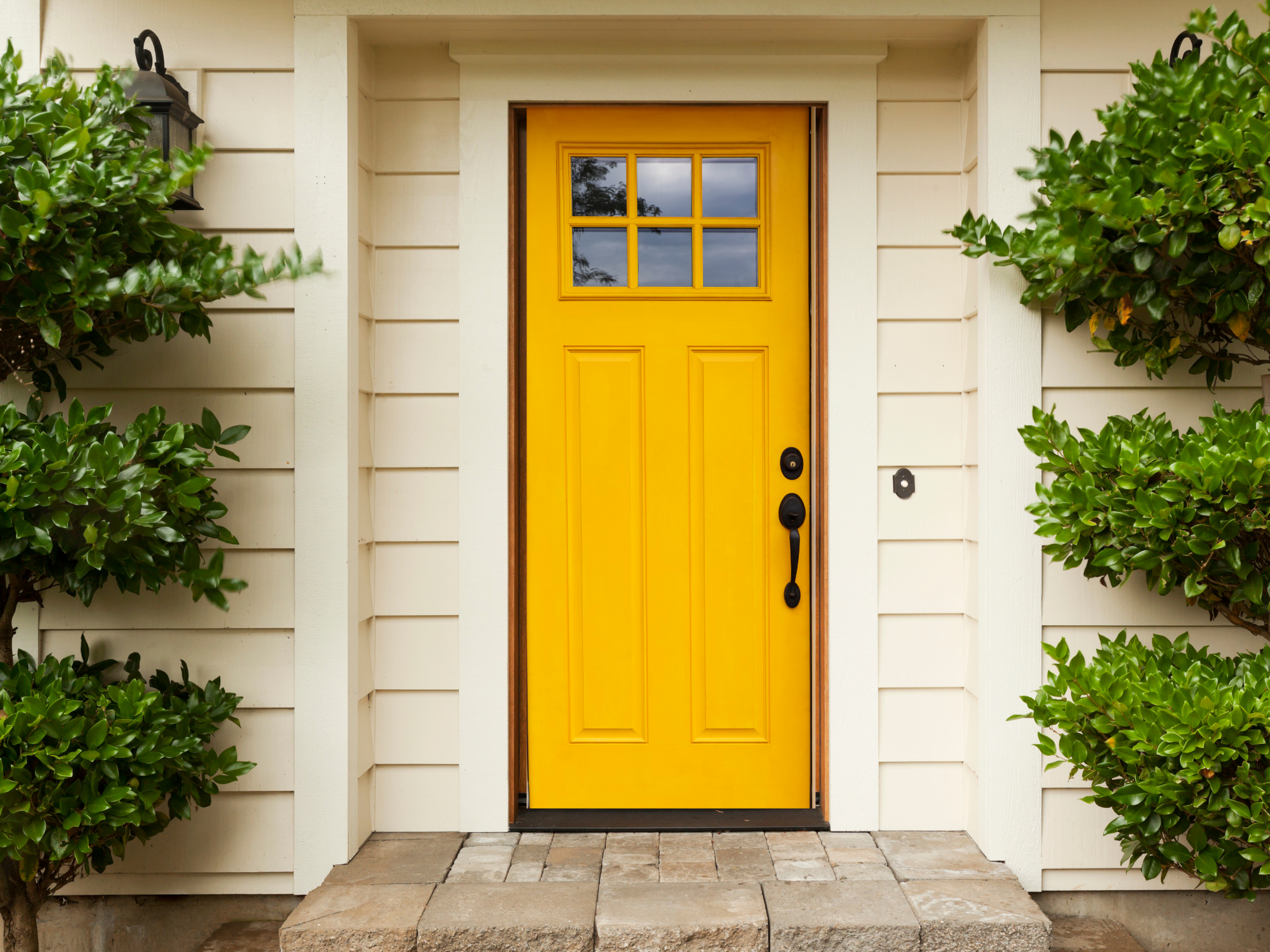 yellow front door creme house green bushes 